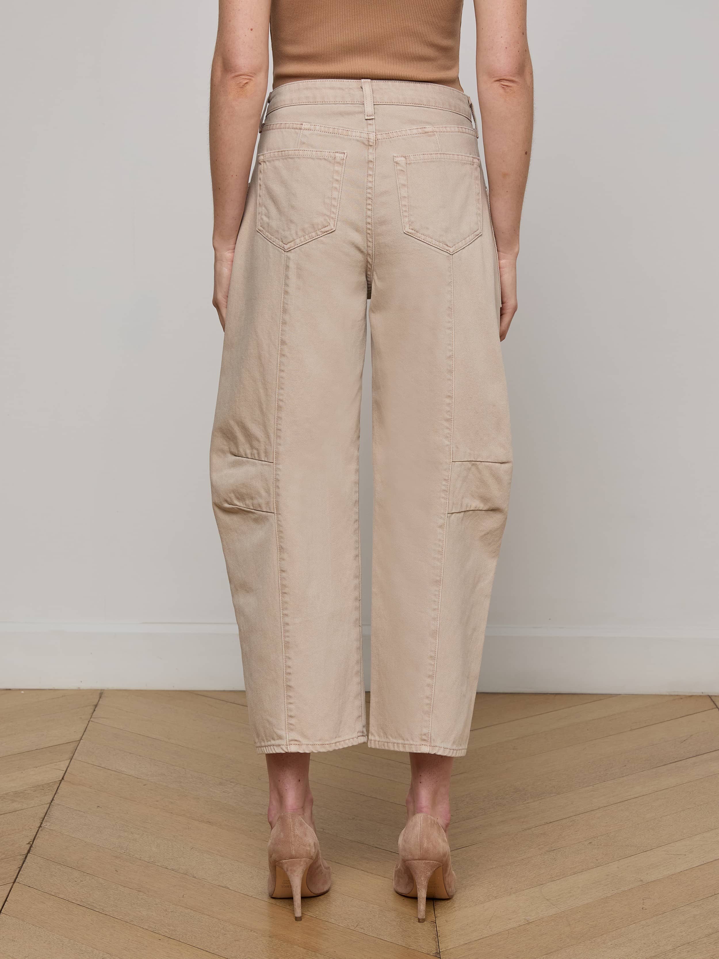 A person wearing the Cody Cropped Barrel-Leg Jean, featuring a beige wide-leg silhouette with patch pockets, paired with tan heels and shown from the back against a plain white background.
