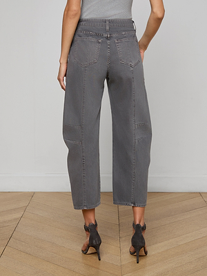 A person stands on a wooden floor, shown from the back, wearing a gray sleeveless top, dark high-heeled sandals, and Cody Cropped Barrel-Leg Jean in high-rise all-cotton denim with wide legs.