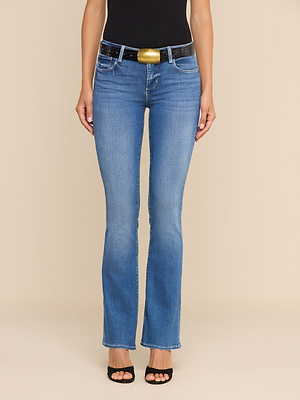 Indossando i jeans Cara a vita bassa e taglio bootcut, un top nero senza maniche, una cintura nera con una grande fibbia dorata e sandali neri con tacco, una persona è in piedi su uno sfondo beige. Il suo volto non è visibile.