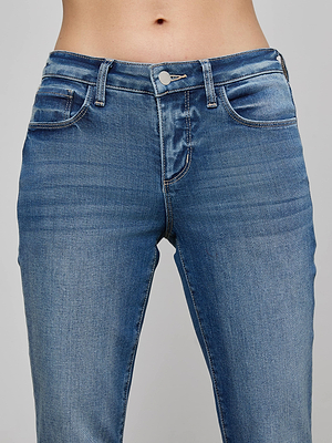 A close-up shows a person wearing the L'AGENCE Cara Low-Rise Bootcut Jean in blue stretch denim with button and zipper closure, highlighting the waistband and upper thighs against a plain background.