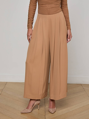 Wearing L'AGENCE Novalynn Cropped Pleated Pant in tan and a long-sleeve ruched brown top, a person stands on a wooden floor; only their body below the shoulders is shown.