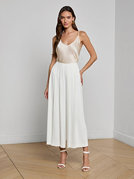 A woman stands against a white background, wearing a sleeveless, light-colored satin top paired with the Novalynn Cropped Pleated Pant and high-heeled sandals.