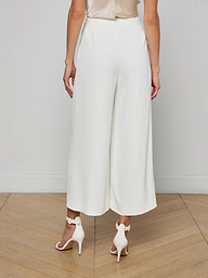 A woman shown from the back against a plain, light background wears the Novalynn Cropped Pleated Pant styled with white high-heeled sandals.