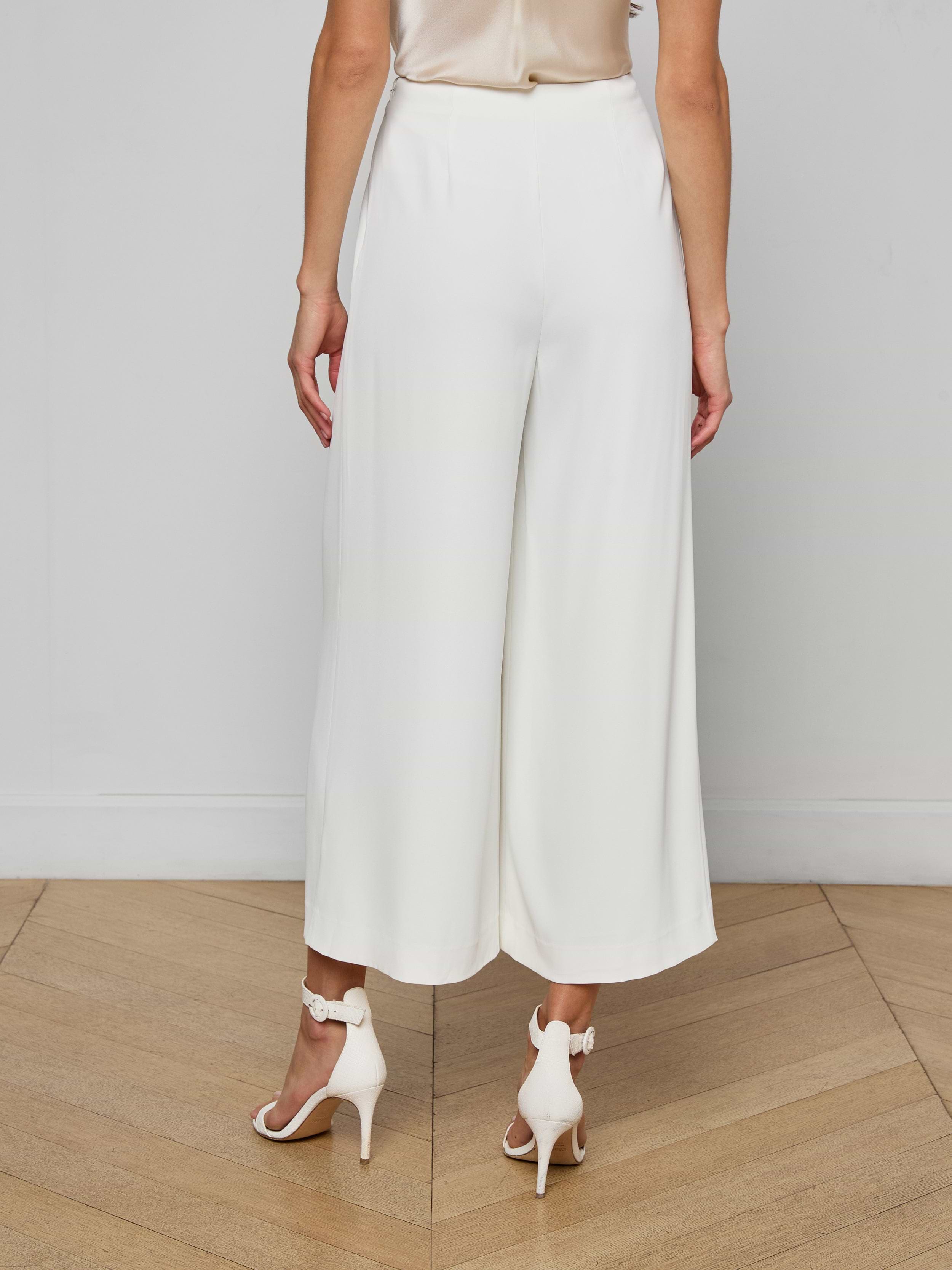 A woman shown from the back against a plain, light background wears the Novalynn Cropped Pleated Pant styled with white high-heeled sandals.