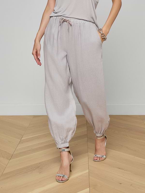 A person wearing light gray Mariko Linen Jogger pants, a matching top, and high-heeled sandals stands against a plain white background.