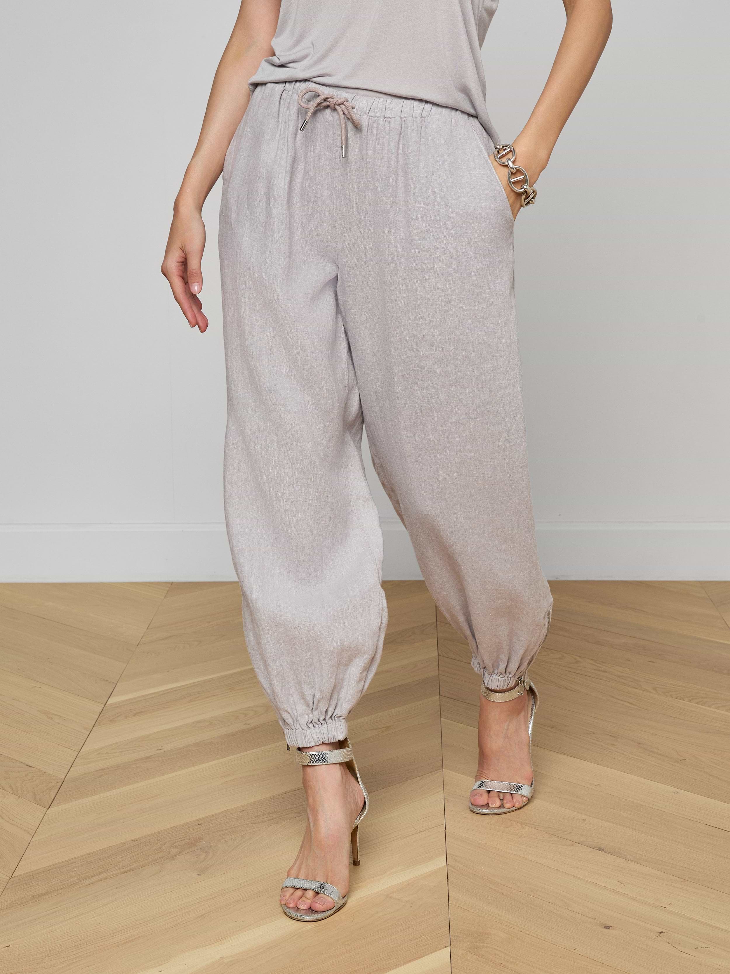 A person wearing light gray Mariko Linen Jogger pants, a matching top, and high-heeled sandals stands against a plain white background.