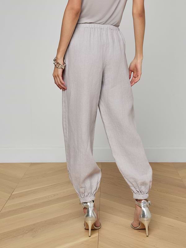 A person is shown from the back against a plain white background wearing the Mariko Linen Jogger in light gray with elastic cuffs and high-heeled sandals.