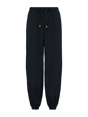 The Mariko Jogger is a black, modern pant made from water-repellent nylon with an elastic waistband, gold-tipped drawstring, relaxed fit, and zip cuffs for versatile styling.