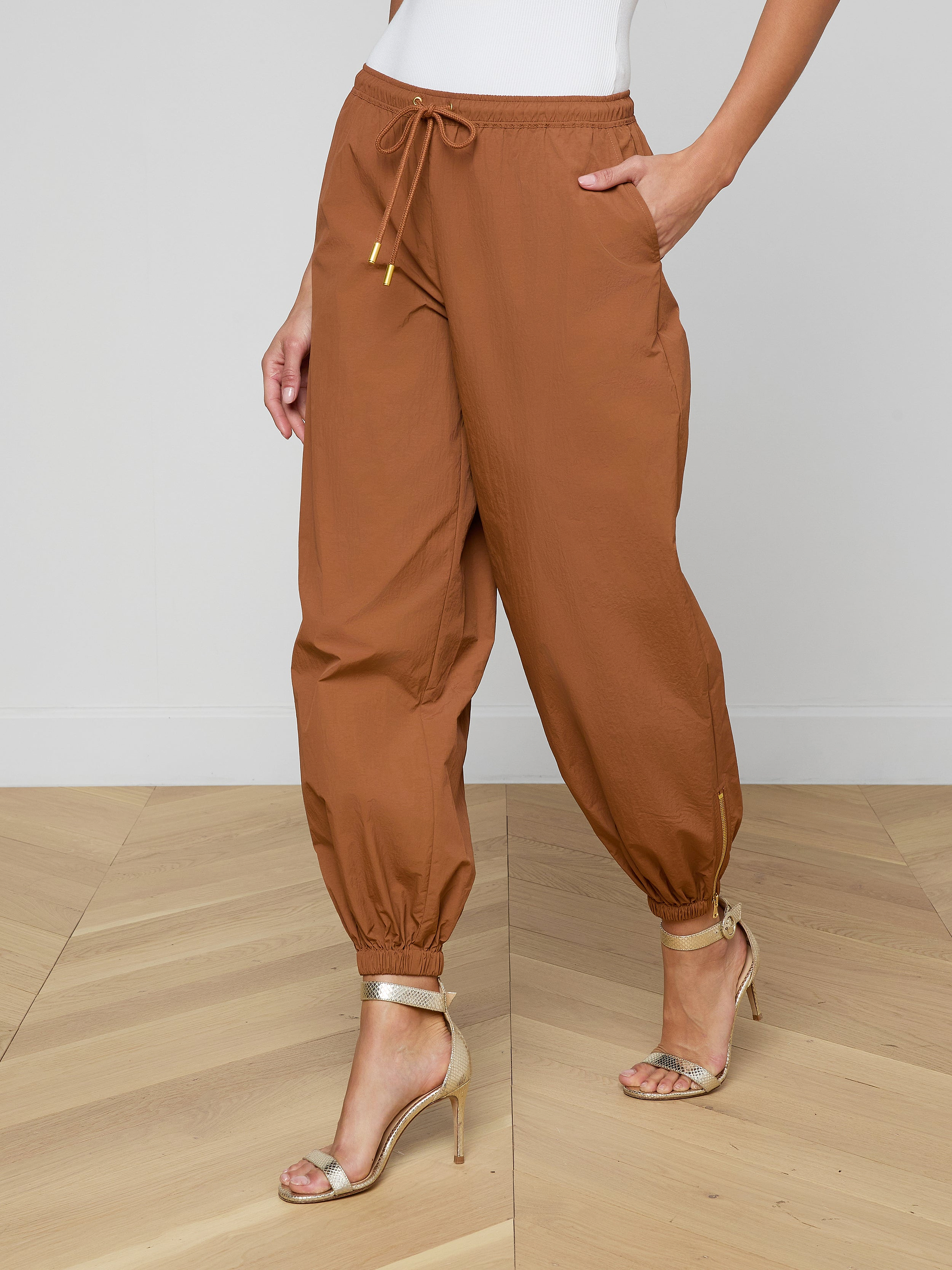 Wearing the Mariko Jogger, a modern brown jogger-style pant featuring ankle cuffs and a drawstring waist, paired with a white top and beige high-heeled sandals.