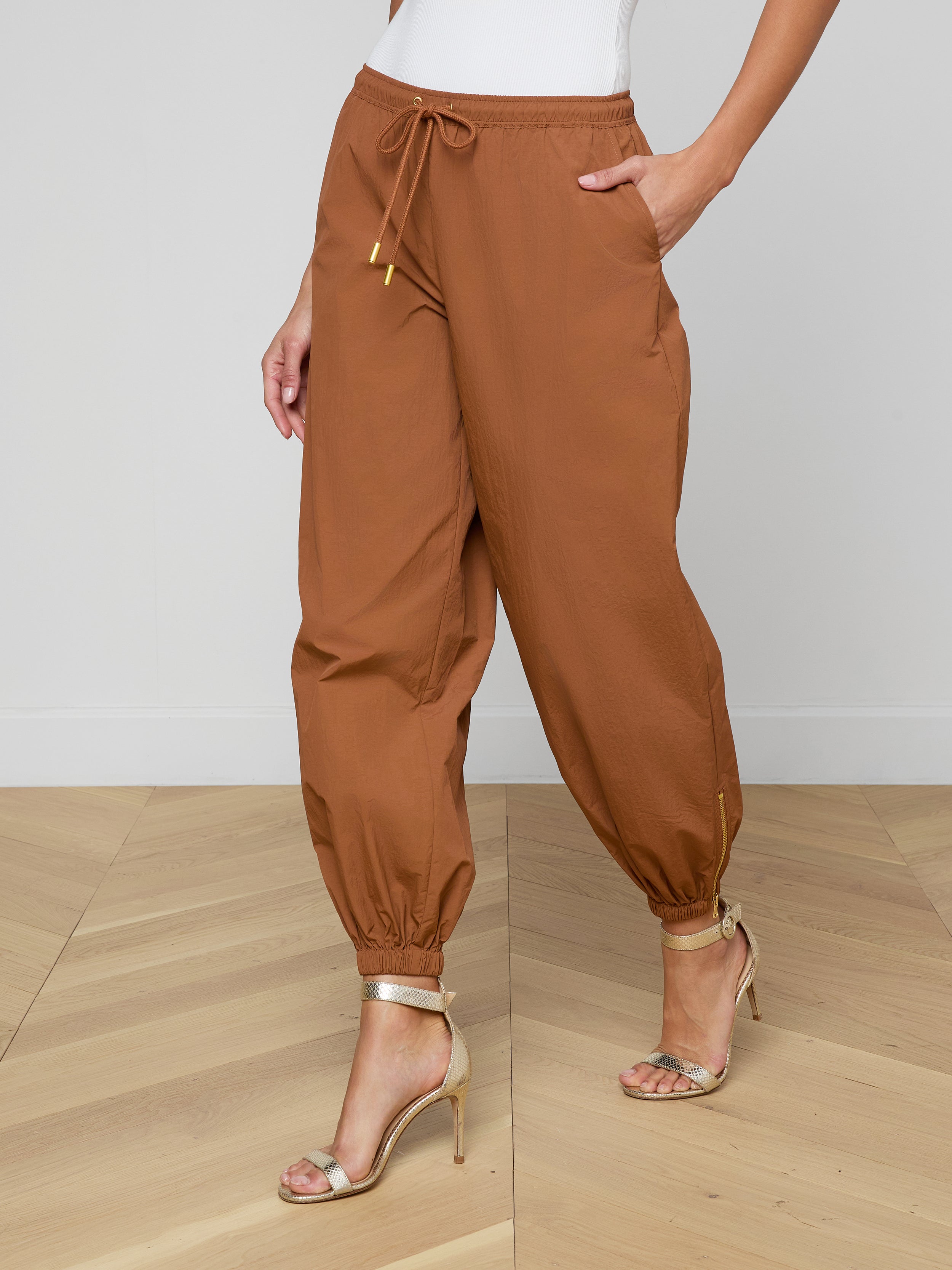 Wearing the Mariko Jogger, a modern brown jogger-style pant featuring ankle cuffs and a drawstring waist, paired with a white top and beige high-heeled sandals.