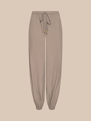 The Mariko Jogger, crafted from lightweight taupe nylon with a water-repellent finish, features gold-tipped drawstrings, elasticated cuffs, and a relaxed fit—shown against a neutral beige background.