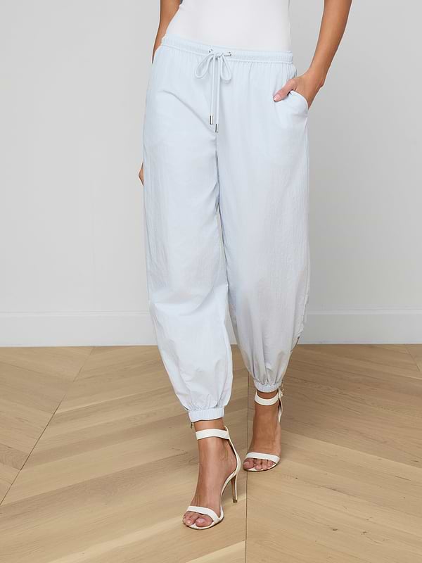 A person wearing the Mariko Jogger in light blue paired with white high-heeled sandals, standing with hands in pockets against a plain light background.