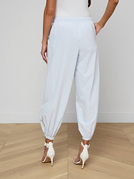A person is shown from the back against a plain background, wearing the Mariko Jogger in light blue—a loose-fitting style with elastic cuffs—paired with white high-heeled sandals.
