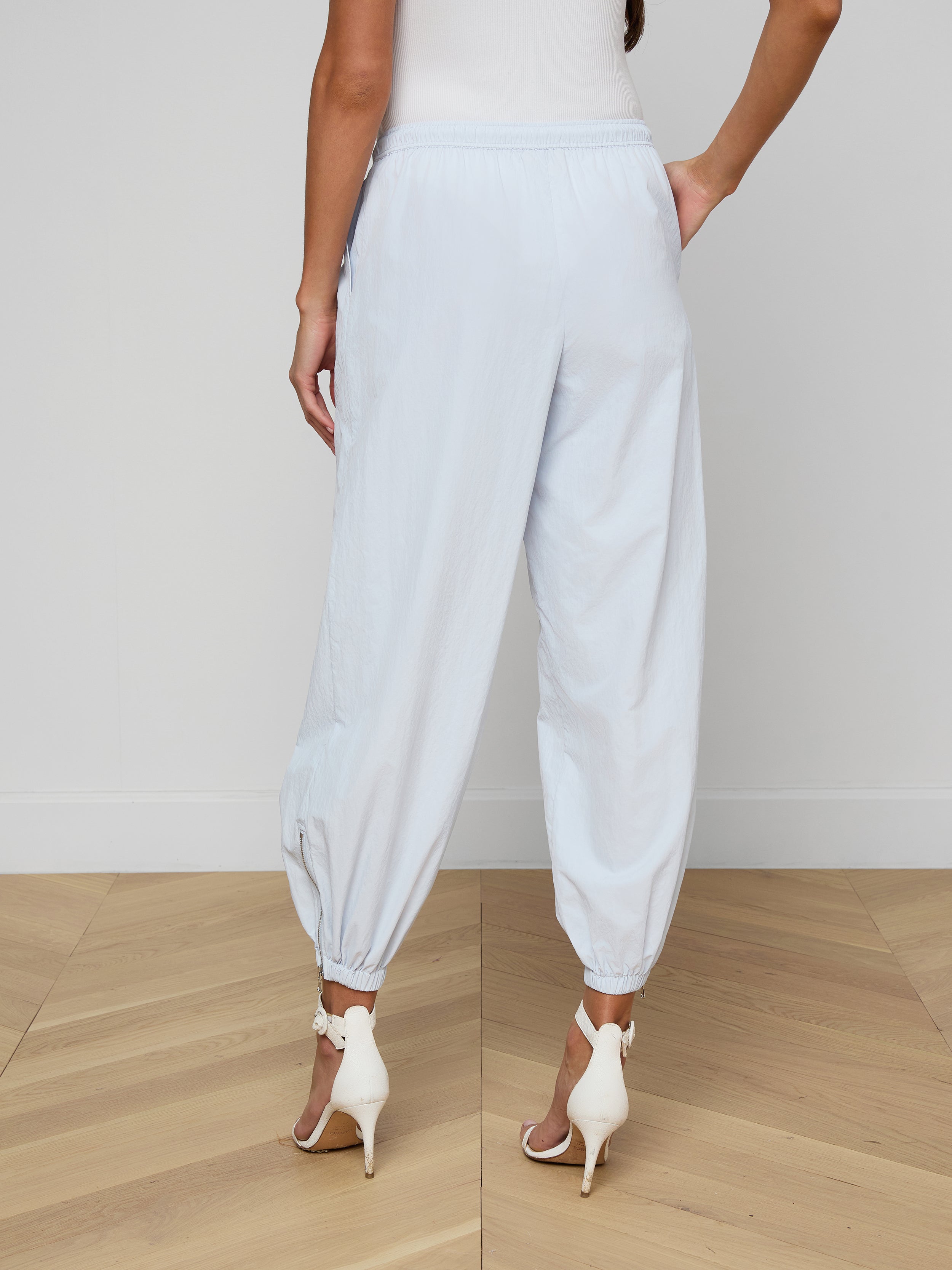 A person is shown from the back against a plain background, wearing the Mariko Jogger in light blue—a loose-fitting style with elastic cuffs—paired with white high-heeled sandals.