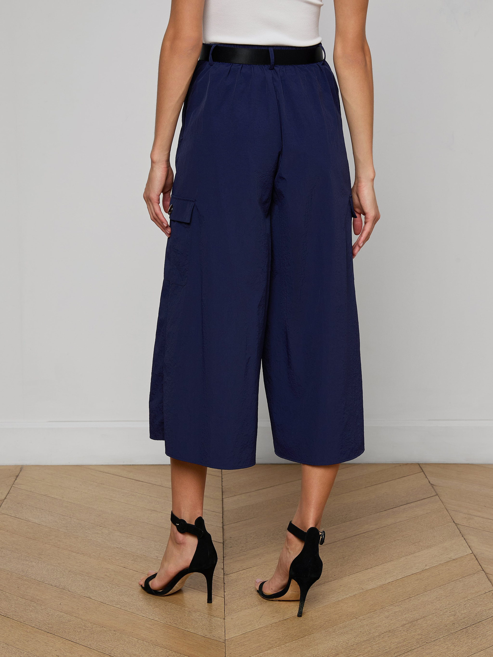 A person is shown from the back against a plain light background, wearing the Shoda Cropped Wide-Leg Pant in navy blue, paired with a white top and black high-heeled sandals.