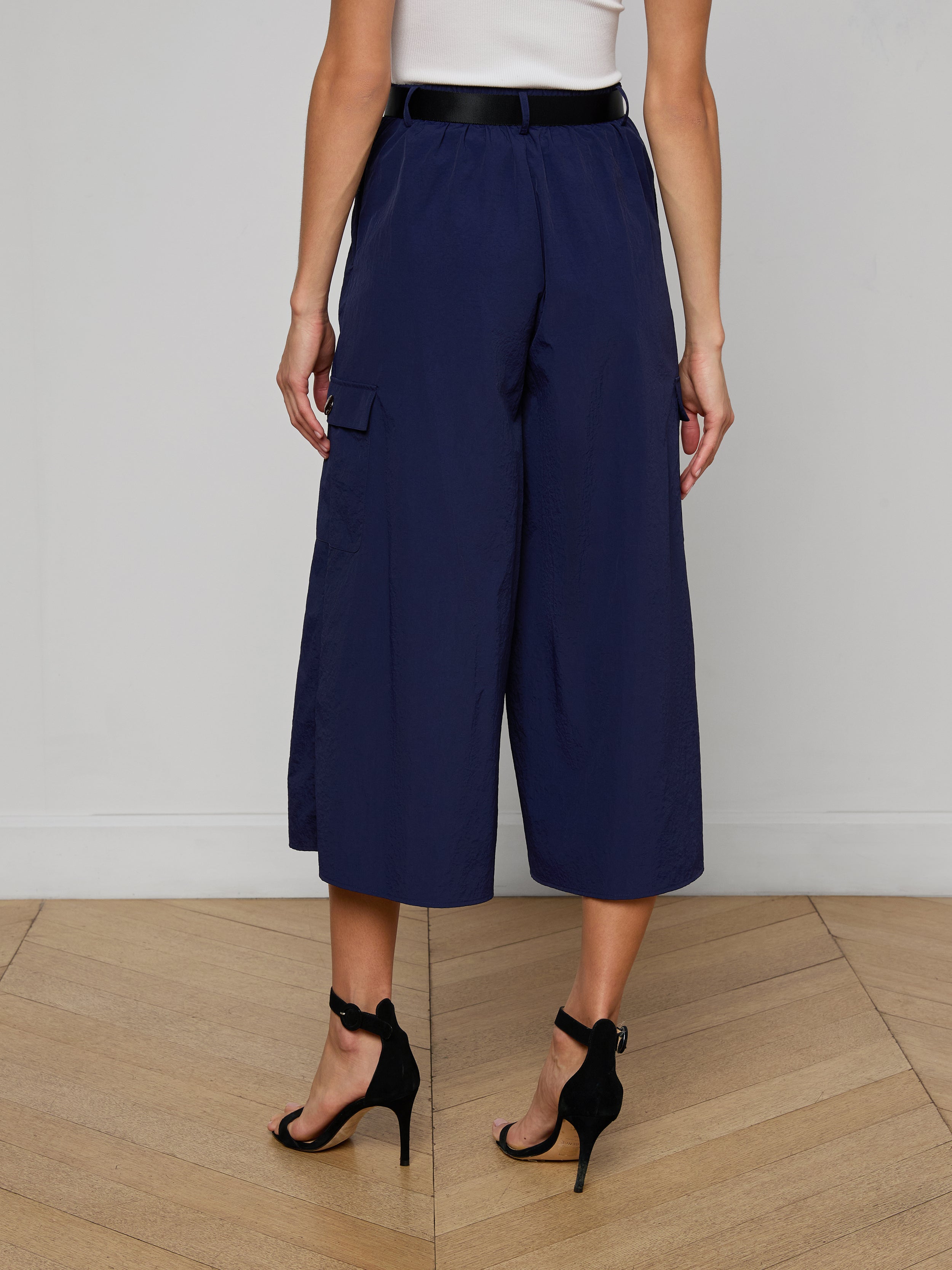 A person is shown from the back against a plain light background, wearing the Shoda Cropped Wide-Leg Pant in navy blue, paired with a white top and black high-heeled sandals.