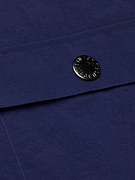 Close-up of the deep blue textured fabric from the Shoda Cropped Wide-Leg Pant, showcasing a shiny round metal snap button closure engraved with text—an element reminiscent of cargo pant detailing that secures an overlapping flap.