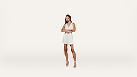 A woman in a sleeveless white dress and white heels stands against a plain white background with her arms crossed and legs slightly apart, looking forward.