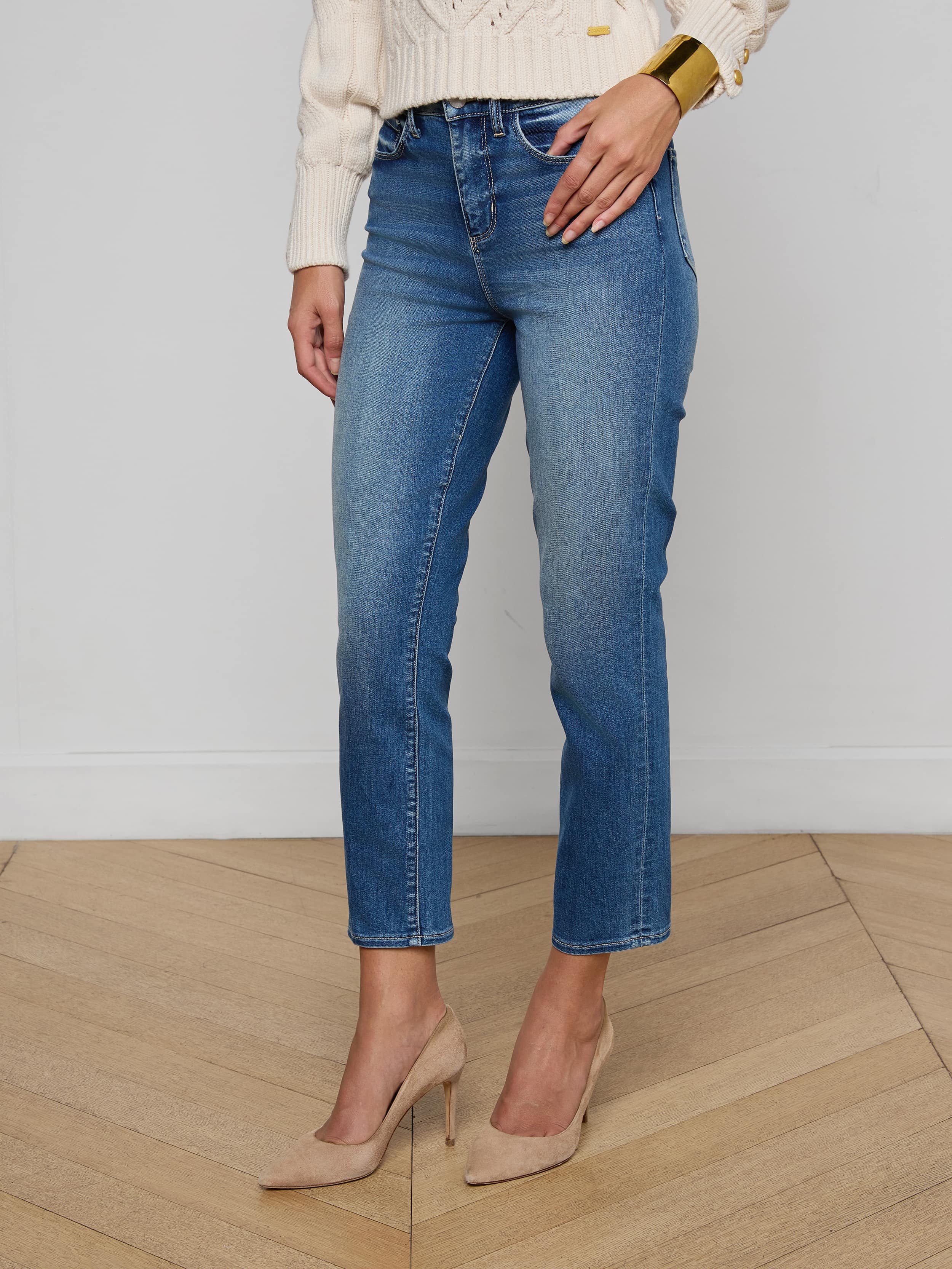 A person wearing the Celestia Slim-Leg Jean in light blue—a high-rise, cropped skinny fit made from stretch denim—paired with a black sleeveless top, a black belt with a gold buckle, and black high-heeled shoes, standing against a plain white background.