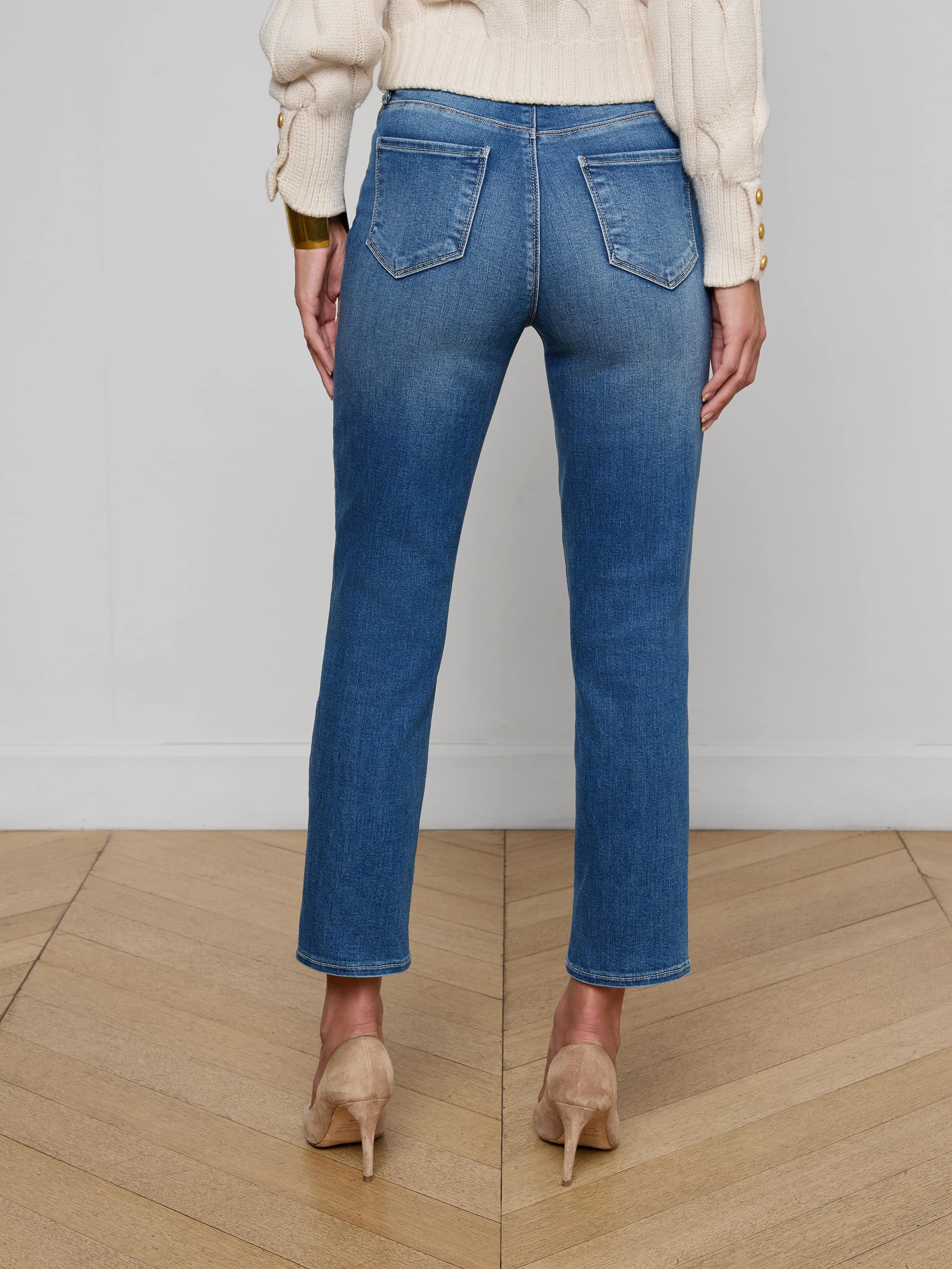 Wearing the Celestia Slim-Leg Jean, black heels, and a black sleeveless top, a person stands facing away from the camera against a plain white background.