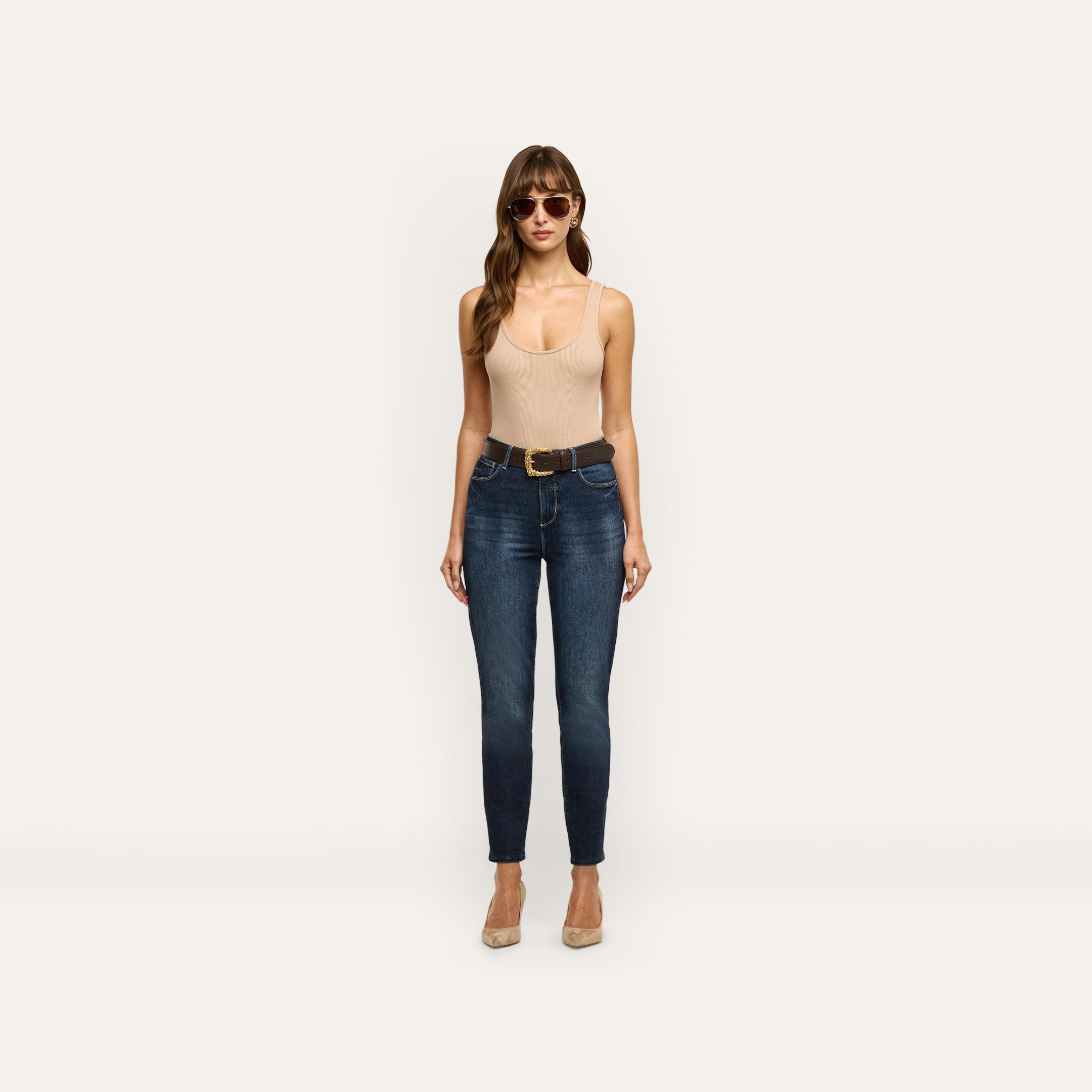 A woman wearing a beige tank top and Celestia Slim-Leg Jean in dark wash denim with a brown leather belt.