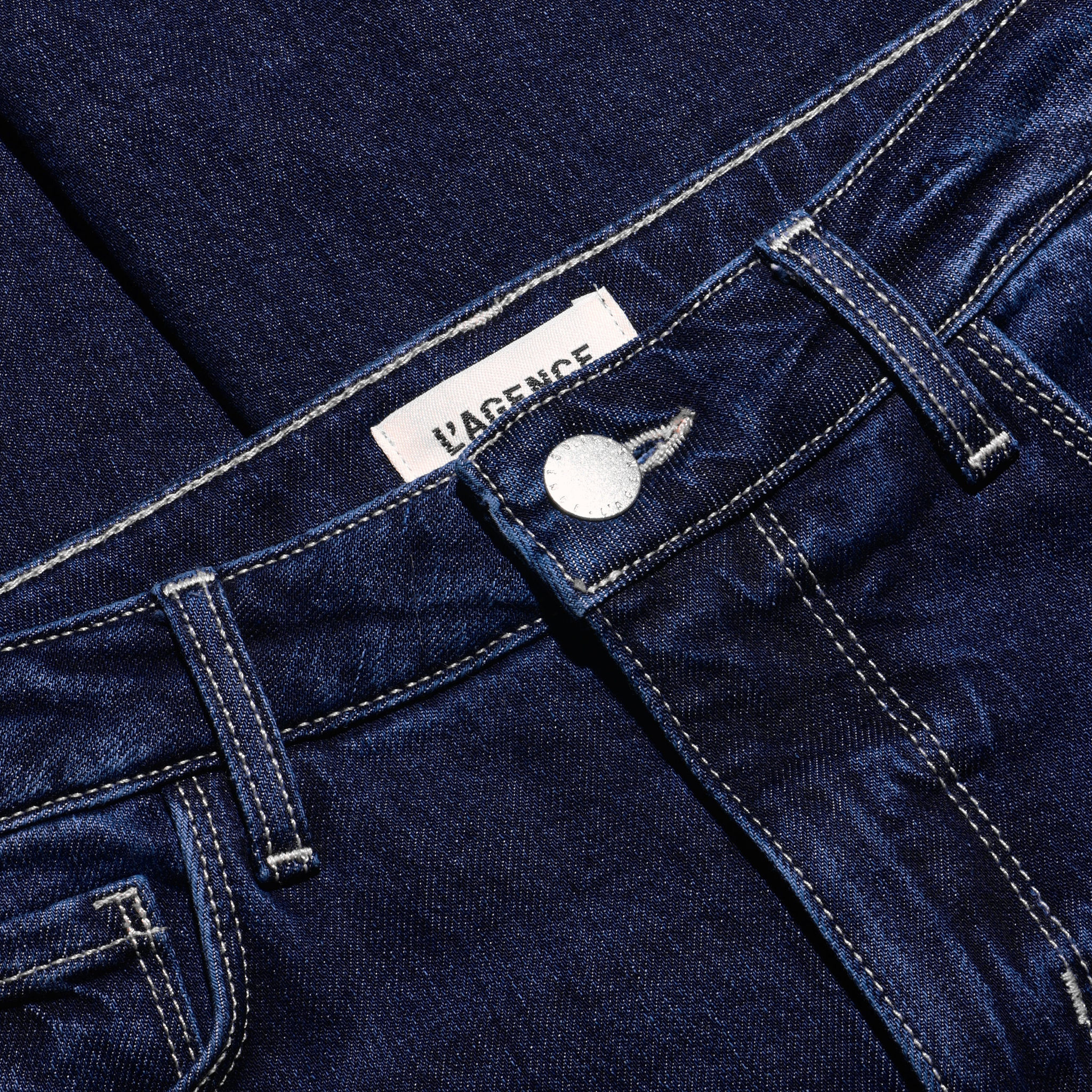 Close-up of Celestia Slim-Leg Jean, featuring a dark wash, ultra high-rise fit, metallic button, and white contrast stitching.