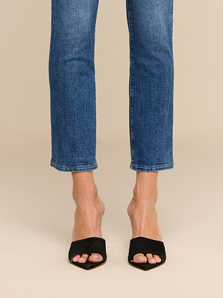 A person wearing the Celestia Slim-Leg Jean in a high rise, indigo wash pairs them with black, open-toe, slip-on heel sandals while standing on a neutral background.