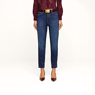A person stands against a beige background, wearing the Celestia Slim-Leg Jean in a classic dark indigo stretch denim, paired with a burgundy lace top and matching burgundy heels; only the lower half of their body is visible.
