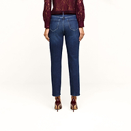 A person wearing the Celestia Slim-Leg Jean in a dark indigo wash, paired with a burgundy lace top and matching burgundy heels, stands facing away to display the back view of their outfit against a plain beige background. The classic stretch denim of the Celestia Slim-Leg Jean offers both comfort and style.