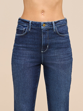 A person wearing the Celestia Slim-Leg Jean in ultra high rise blue with white stitching, crafted from classic stretch denim, shown from the waist to mid-thigh against a plain beige background.