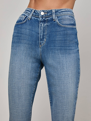 Close-up of a person wearing the L'AGENCE Celestia Slim-Leg Jean featuring high-rise, button and zipper closure, front pockets, and subtle thigh fading. Only the torso is visible; these relaxed jeans offer timeless style.