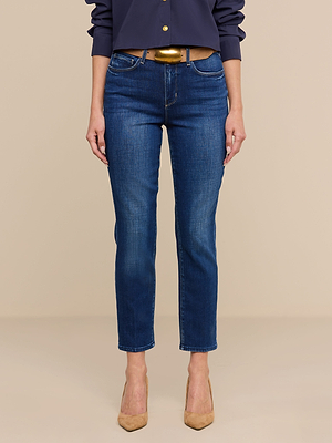 A person stands against a plain beige background, shown from shoulders to feet with arms relaxed, wearing Celestia Slim-Leg Jeans in ultra high rise blue, a navy long-sleeve shirt, and beige pointed-toe heels.