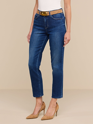 Eine Person, die eine blaue „Celestia Slim-Leg“-Jeans, einen hellbraunen Gürtel, ein weißes Oberteil und hellbraune Schuhe mit hohen Absätzen trägt, steht vor einem beigen Hintergrund.