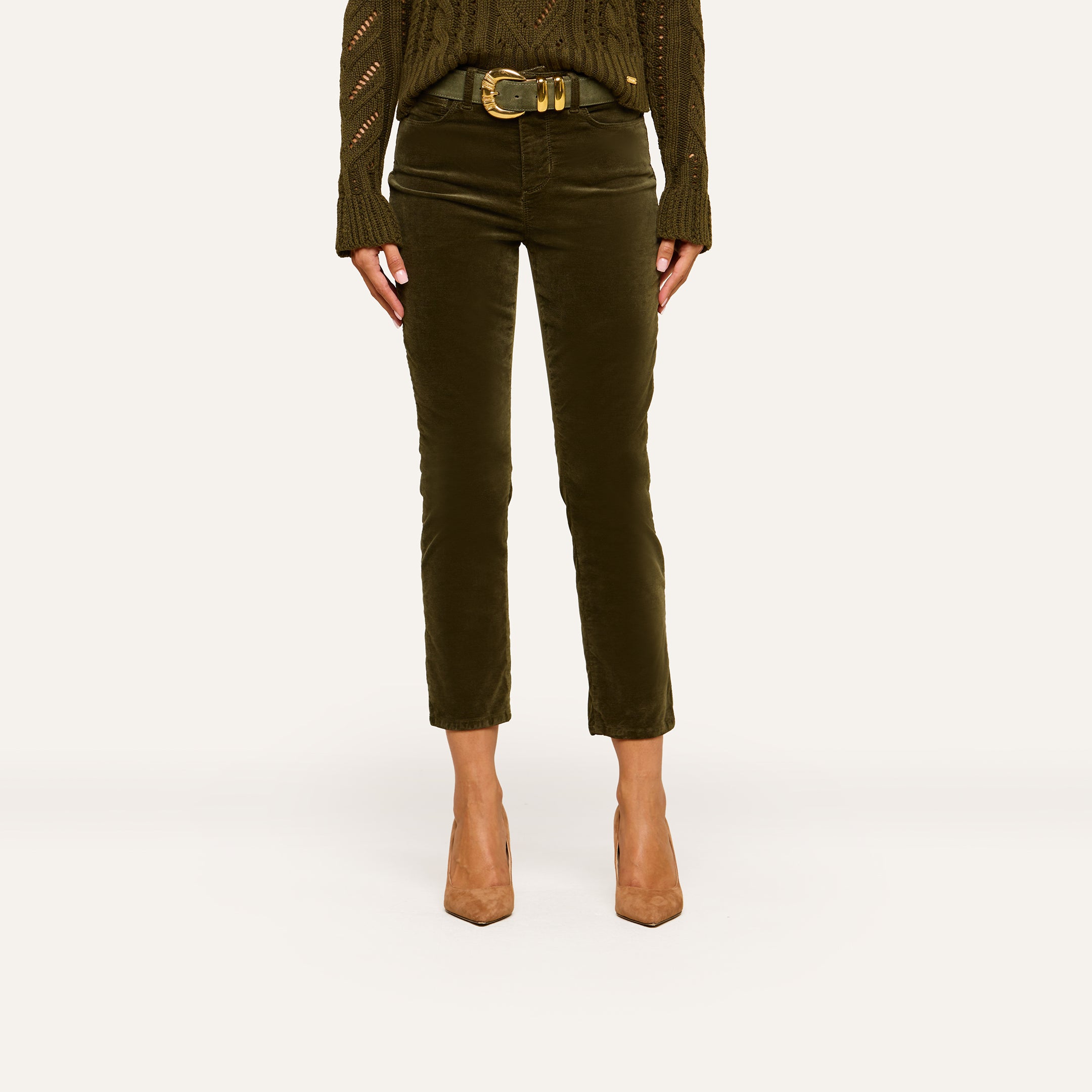 A person wearing the Celestia Velvet Slim-Leg Jean in olive green with a matching knit sweater, a wide belt, and tan pointed-toe heels, shown from shoulders down against a plain background.