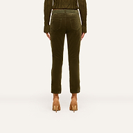 A person stands facing away against a plain background, showcasing the back view of the outfit featuring the Celestia Velvet Slim-Leg Jean in dark green, paired with a matching knit sweater and tan high heels.