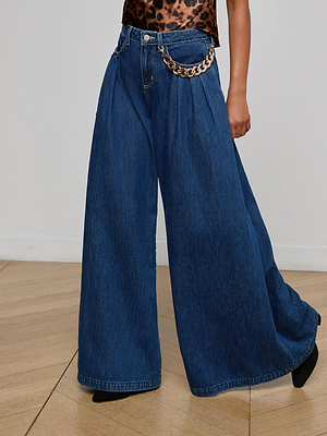 Someone stands on a light wood floor against a white wall, wearing the L'AGENCE Chayse Wide-Leg Jean in non-stretch denim with pleats, a statement chain belt, and a leopard print top.