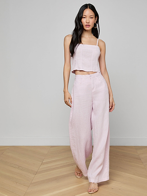 A woman with long dark hair poses indoors on a light wood floor against a plain wall, wearing sandals and the Amara Linen Wide-Leg Pant in light pink with a matching sleeveless crop top.