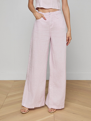 Someone wears the Amara Linen Wide-Leg Pant in light pink with a matching cropped top, standing on a wooden floor against a plain light wall. Their left hand is in their pocket and their face is out of view.