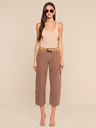 A woman with long hair, wearing sunglasses, a beige tank top, the high-rise brown Mallis Corduroy Bow-Leg Pant, and open-toe heels stands against a plain white background.