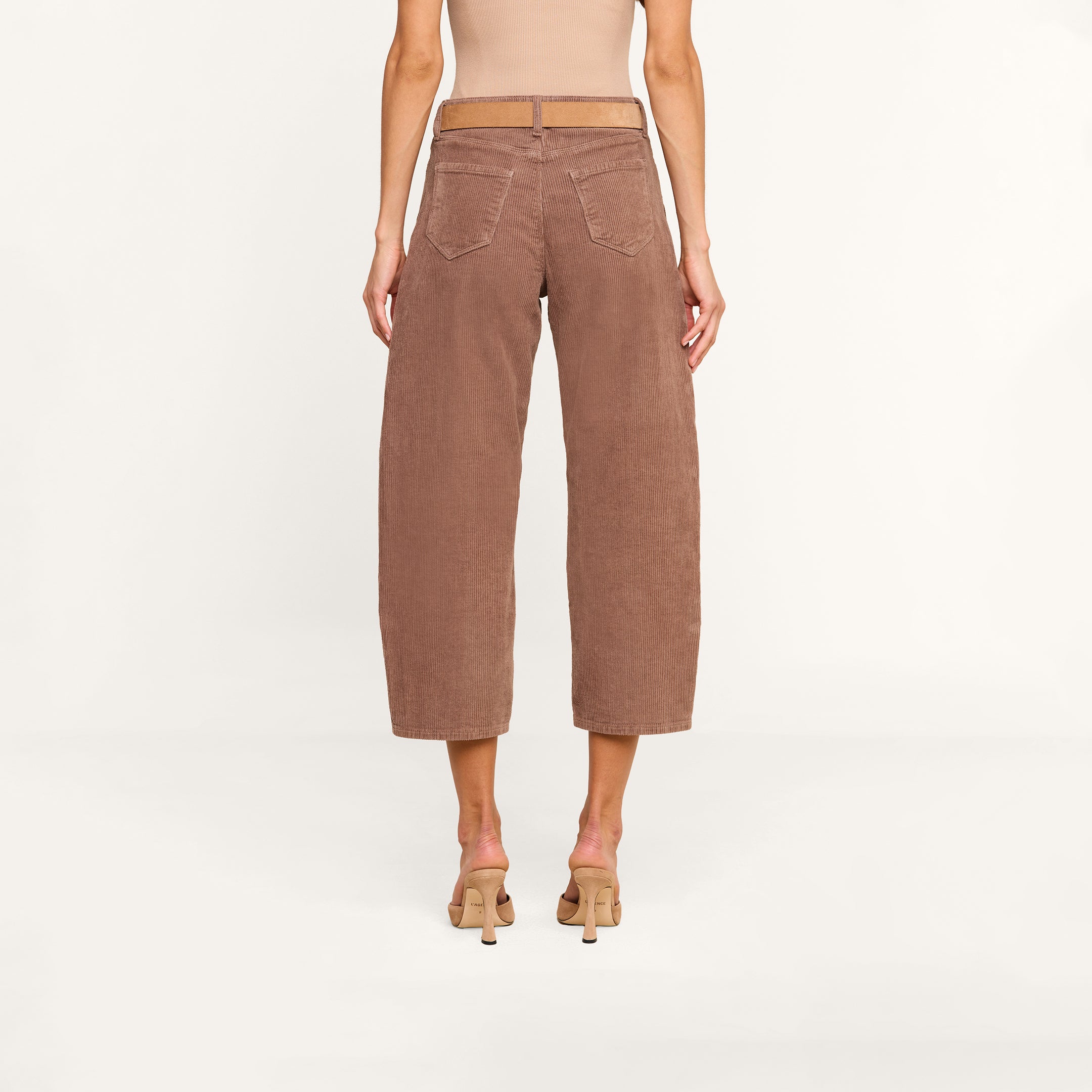 A person is shown from the back, standing against a plain white background, wearing the Mallis Corduroy Bow-Leg Pant in brown styled with beige heels.