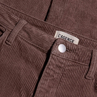 Close-up of the Mallis Corduroy Bow-Leg Pant in brown, featuring a high rise, visible button, front pocket, and a label reading LAGENCE above the waistband.