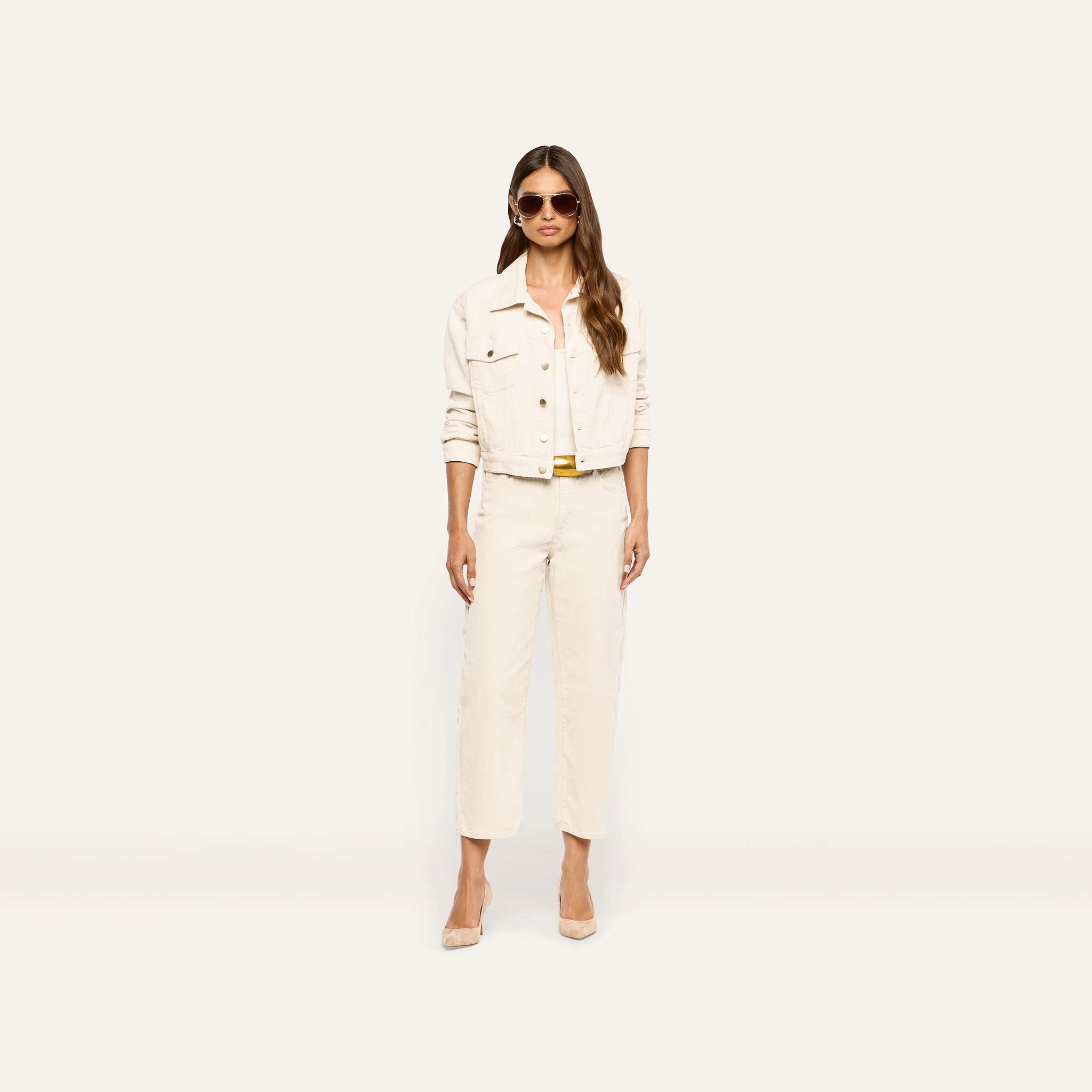 A person wearing a cropped cream jacket, matching high-rise cream Mallis Corduroy Bow-Leg Pant, and tan heels.