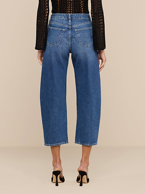 A person is shown from the back wearing Mallis Bow-Leg Jeans—high-rise, all-cotton, wide-leg blue cropped denim—paired with black high-heeled sandals and a black long-sleeve knit top against a plain beige background.