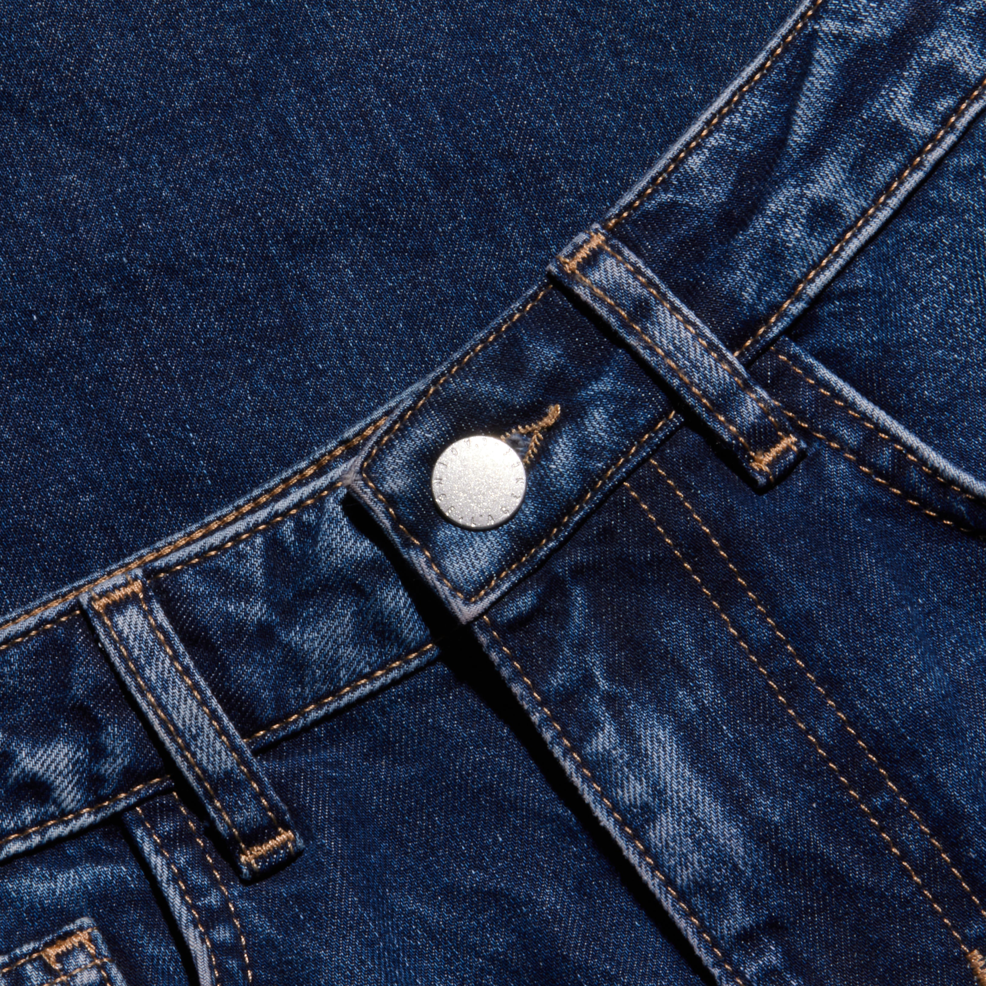 Close-up of dark blue denim jeans showcasing the waistband, belt loops, metal button, and distinctive orange stitching details.