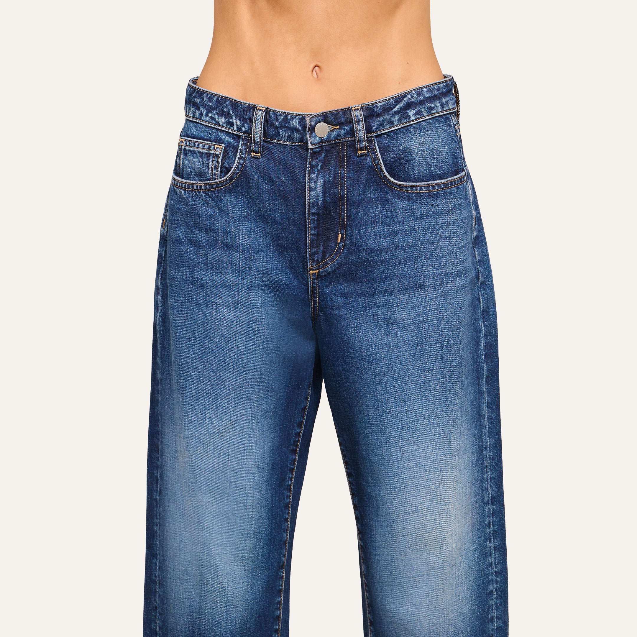 A person wearing high-waisted, blue denim jeans with a button closure and front pockets, styled in a modern silhouette from the waist to mid-thigh.