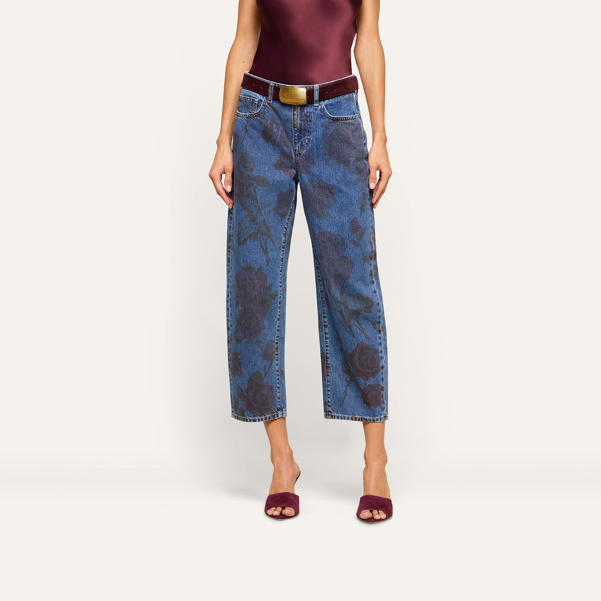 Wearing the Mallis Bow-Leg Jean, which features a wide-leg silhouette and rose print, this person pairs it with a dark red sleeveless top, a brown belt, and matching dark red open-toe heels against a plain light background.