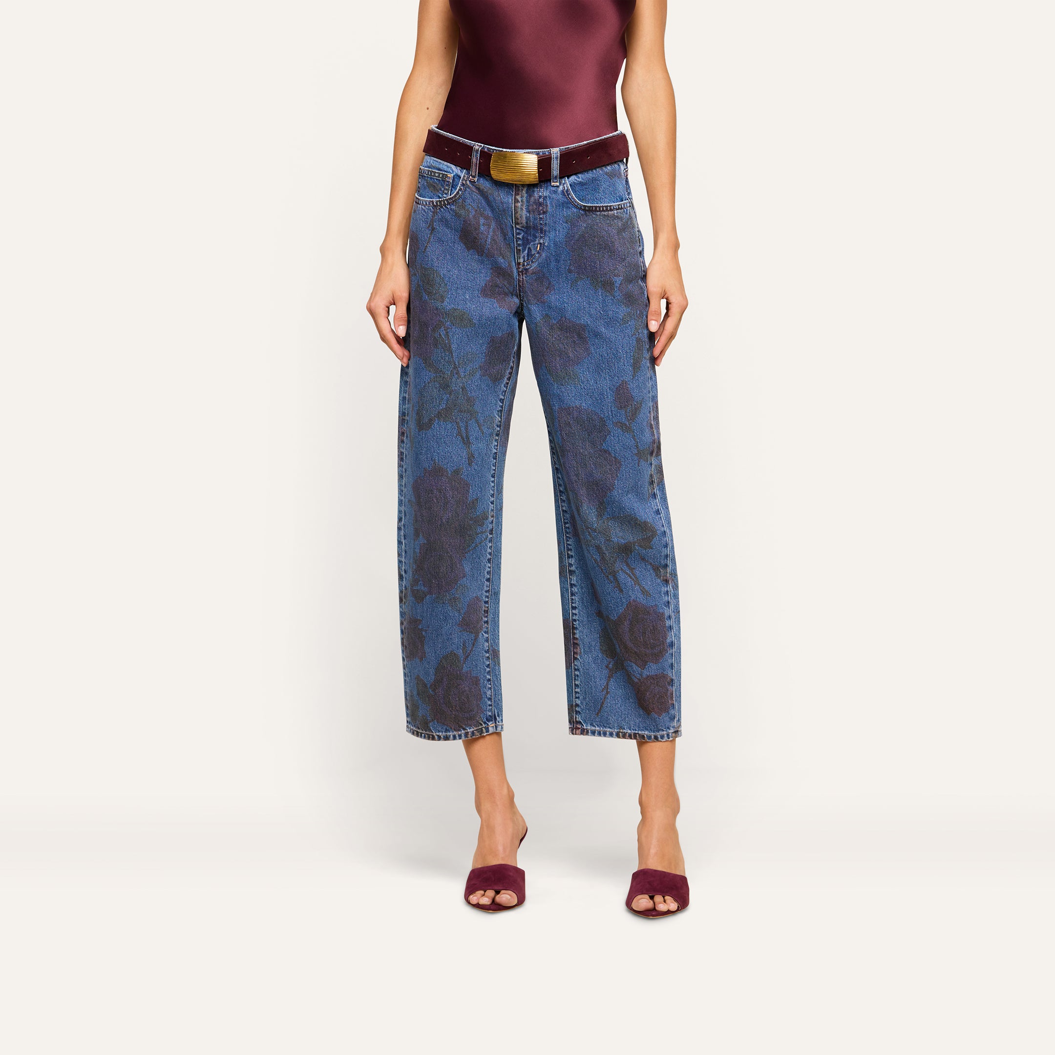 Wearing the Mallis Bow-Leg Jean, which features a wide-leg silhouette and rose print, this person pairs it with a dark red sleeveless top, a brown belt, and matching dark red open-toe heels against a plain light background.
