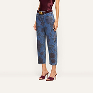 A person wearing a sleeveless burgundy top and the Mallis Bow-Leg Jean, featuring a rose print and wide-leg silhouette with a black belt, pairs the look with matching burgundy heeled sandals while posing against a plain background.
