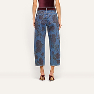 A person seen from the back wearing the Mallis Bow-Leg Jean, featuring a cropped blue denim with a dark rose print, styled with burgundy high-heeled shoes and a sleeveless burgundy top.