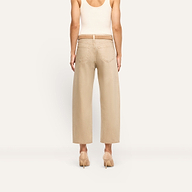 Back view of a person wearing Mallis Coated Bow-Leg Jean in beige, featuring a high-rise, wide-leg cut with a thin belt and pointed-toe heels.
